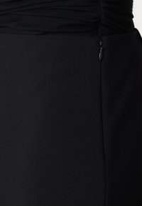 Robe noire dotée d'une partie inférieure ajustée et d'une partie supérieure froncée et texturée. Comprend une fermeture éclair latérale discrète. Fabriquée en tissu lisse.