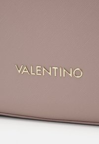 Růžová texturovaná kůže se zlatým logem "Valentino", s hladkým povrchem a čistými liniemi, zdůrazňující minimalistický design značky.