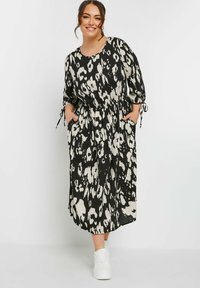 Svartvit leopardmönstrad klänning med lös passform, långa ärmar, elastisk midja och sidfickor, kombinerad med vita sneakers.