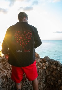 Črna denim jakna z obliko srca, ki je sestavljena iz rdečih in roza src; z napisom "SWEET heart" v beli in rdeči barvi. Oblečena je čez rdeče kratke hlače.
