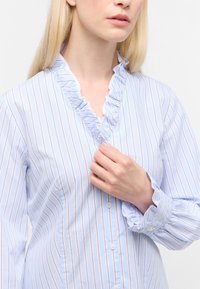 Camicia a righe blu chiaro con collo e polsini arricciati. Realizzata in cotone, presenta righe bianche e arancioni, e bottoni frontali. Tessuto morbido.