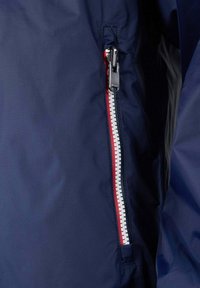 Marineblaue Jacke mit diagonalem, wasserdichtem Reißverschluss und einem weißen sowie roten Zugband. Glatte Stofftextur mit dezentem Karomuster.