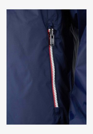 Chaqueta azul marino con cremallera impermeable diagonal y pestaña blanca y roja. Textura de tela lisa con un sutil patrón de cuadricula.