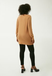 Tan langærmet sweater med afslappet pasform, ribbede manchetter og rund kant, parret med sorte leggings og sorte chunky hælsandaler.