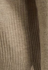 Beżowy sweter dziany o fakturze prążkowanej, z pionowymi pasami i gładkim wykończeniem. Materiał wygląda na miękki i wygodny.