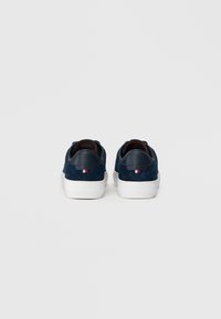 Baskets en daim bleu marine avec un talon en cuir bleu marine lisse et une semelle en caoutchouc blanc, présentant un petit accent rouge, blanc et bleu à l'arrière.
