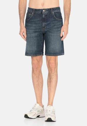 Shorts de mezclilla en azul oscuro, corte recto, con cinco bolsillos, cierre de botón en la parte superior y dobladillo sin acabar. Llevados con zapatillas deportivas blancas.