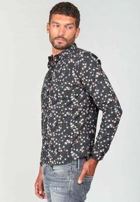Camisa de manga larga negra con un patrón de flores y acentos en blanco y naranja, hecha de una tela ligera y suave. Detalles personalizados en los botones.