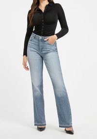 Black long-sleeve button-up top with ruching detail, paired with light blue, high-waisted, wide-leg jeans and black pointed-toe heels.
