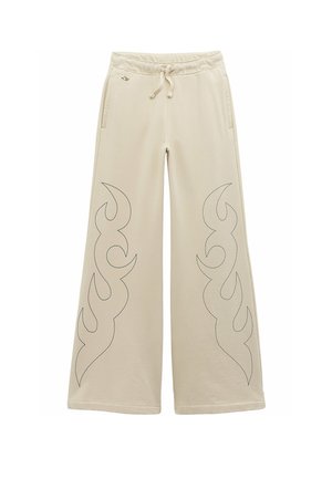 Pantalones beige de pierna ancha con cintura ajustable con cordón, bolsillos laterales y patrones cosidos en forma de llamas negras en la parte delantera de las piernas.
