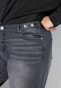 Czarne jeansy slim-fit wykonane z denimu, charakteryzujące się gładką fakturą, srebrnymi guzikami oraz subtelnymi pionowymi paskami po bokach.