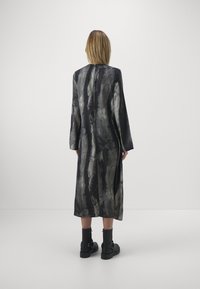 Rochie lungă din țesătură neagră și gri cu un model, cu croi drept, mâneci lungi și fante laterale, asortată cu cizme negre până la glezna.