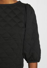 Svart vadderad topp med rund halsringning, puffade trekvartsärmar och en strukturerad diamantmönster över hela.