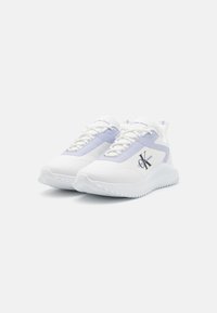 Baskets de sport blanches et lavande avec une tige lisse, un détail de logo, une semelle texturée et un système de laçage. Design minimaliste.