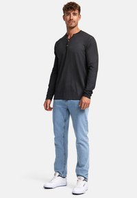 Dunkelgraues, langärmliges Henley-Shirt mit drei braunen Knöpfen, kombiniert mit hellblauen Jeans und weißen Sneakern. Lässiger Schnitt, bequemer Stoff.