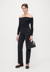 Juoda kūno suit su atvirais pečiais derinama su tamsiomis džinsomis. Juoda rankinė su grandinėlių akcentais. Masyvūs rudi platforminiai bateliai. Lygūs tekstūriniai paviršiai.