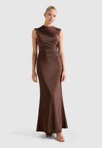 Bronzas krāsas, bezroku maksi kleita ar rušēšanu un pieguļošu siluetu. Gluda, mirdzoša auduma virsma plūst uz nedaudz paplašinātu apmali.