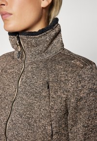 Fleece zipjakke i brun og sort tekstur, med høyt krage, sidelommer med glidelås, og tonale sømdetaljer.
