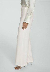 Szerokie spodnie w jasnym kremowym kolorze, wykonane z gładkiego materiału o czystych liniach. Połączone z srebrnymi sandałami na obcasie dla formalnego wyglądu.