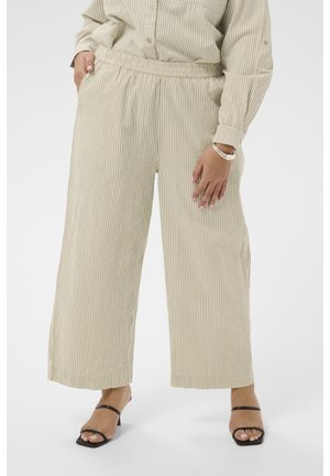 Pantalon large à rayures verticales beige et blanc, assorti avec une chemise assortie, porté avec des talons ouverts noirs et un bracelet argenté.
