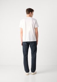 White cotton t-shirt with short sleeves, paired with dark blue denim jeans. The jeans feature classic back pockets and a straight-leg fit.