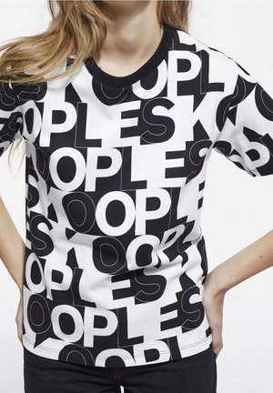 Personne portant un T-shirt noir et blanc avec de grandes lettres superposées formant le mot "PEOPLE" dans un motif audacieux.