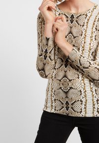 Bluzka z długim rękawem z wzorem w beżowe i brązowe węże, z okrągłym dekoltem, wykonana z gładkiej, elastycznej tkaniny.