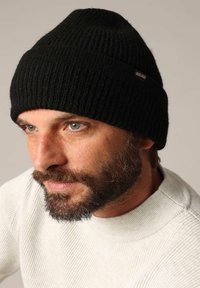 Zwarte geribbelde gebreide beanie met een opvallend logo label. De textuur is zacht en rekbaar, ontworpen voor een snuggy pasvorm.