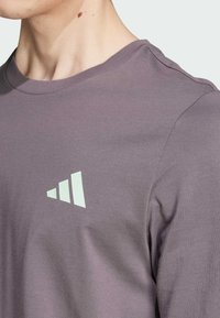 Camisa de manga larga gris hecha de tela suave, con un cuello redondo y un logotipo geom�étrico verde claro en la parte superior izquierda.