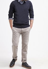 Maglione blu marina su una camicia a quadri, pantaloni beige e stivali neri. Presenta un design a V, maniche arrotolate e orli dei pantaloni risvoltati.