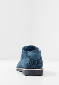 Bottine en daim bleu avec texture perforée, semelle en caoutchouc et coutures contrastantes. Forme arrondie, doublure intérieure lisse, design minimaliste.