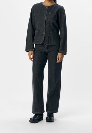 Person wearing black denim jacket with front buttons, three patch pockets, matching straight-leg jeans, and black platform shoes.