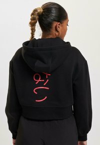 Black cropped hoodie with a drawstring hood. Features a bold red graphic design on the back. Soft fabric with ribbed cuffs and hem.