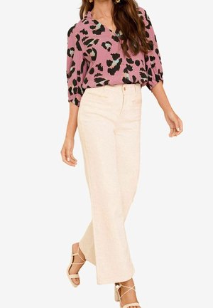 Vrouw draagt een mauve luipaardprint blouse met driekwart mouwen, crème hoge taille wijde broek en beige sandalen met bandjes.