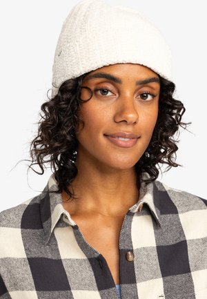 White knit beanie with a textured design, worn with a black and white checkered shirt. Features a simple, casual appearance.
