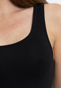 Top in cotone nero senza maniche con spalline larghe, scollatura rotonda e una texture liscia e opaca. Caratterizzato da cuciture rinforzate lungo i bordi.