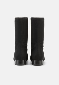 Μαύρα μποτάκια μέχρι τον αστράγαλο με λείο, ελαστικό ύφασμα στην επάνω πλευρά. Διαθέτουν στρογγυλεμένη μύτη και χαμηλό τετράγωνο τακούνι. Απλός σχεδιασμός, χωρίς ορατά σχέδια ή διακοσμήσεις.