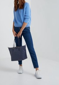 Light blue knitted sweater, dark blue fitted jeans, and a navy polka dot tote bag with gold hardware. White sneakers complete the outfit.