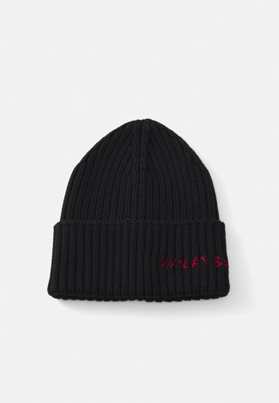 Zwarte gebreide beanie met een geribbelde textuur en een omgeslagen rand. Heeft rode geborduurde tekst op de rand. Zacht, warm materiaal.