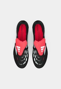Μαύρα αθλητικά παπούτσια με υφή στην επάνω επιφάνεια, έντονες κόκκινες λεπτομέρειες και λευκές ρίγες. Κομψός σχεδιασμός με ανοικτό πλέγμα και ξεχωριστές λεπτομέρειες.