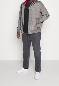 Šedá bomber bunda s červeným límcem, doplněná o námořnické tričko, šedé džíny a bílé tenisky. Obsahuje boční kapsy a elastické manžety.