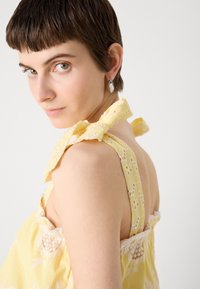 Robe jaune avec des rayures verticales, ourlet en dentelle et détails en nœud sur l'épaule. Présente un dos nu et un tissu texturé.