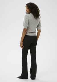 Pull gris ajusté avec une finition texturée et des manches bouffantes, associé à un pantalon noir évasé, présenté de dos sur un fond uni.