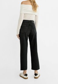 Vaqueros negros de cintura alta con un diseño de pierna ancha, que cuentan con bolsillos traseros y un dobladillo sin rematar, combinados con una blusa de manga larga ligeramente off-shoulder.