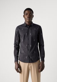 Camicia nera a maniche lunghe con strisce verticali bianche e delicati ricami floreali. Design fitted e colletto a punta.