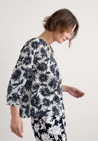 Schwarz-weiße Bluse mit floralen Mustern, dreiviertelärmlig, mit V-Ausschnitt und leichtem Stoff. Kombiniert mit passenden gemusterten Hosen.