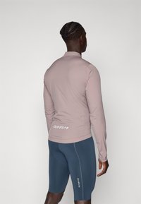 Maglietta a maniche lunghe rosa chiaro con design aderente, texture liscia e logo bianco sul retro. Pantaloni corti blu coordinati con branding simile.
