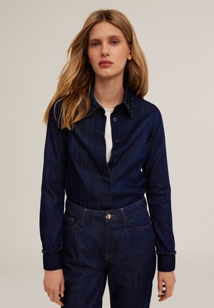 Donkerblauwe spijkerblouse met een knoopsluiting aan de voorkant, versierde kraag en manchetten met decoratieve studs. Aansluitende pasvorm, gladde textuur.