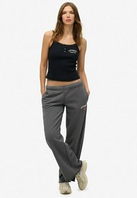 Zwarte nauwsluitende tanktop met een ronde halslijn en decoratieve kantafwerking, gecombineerd met grijze losse sweatpants met zijzakken en een logo.