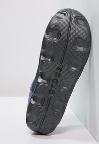 Černá gumová podrážka boty Crocs, s texturovaným povrchem a vlnkovým vzorem, a výrazným logem vyraženým na boku.